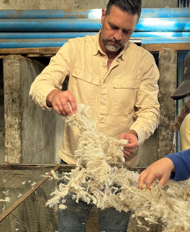 Man examining raw wool in a farm setting, part of the making of process.